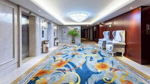 Eine Hotelhalle mit einem langen, verzierten Teppich, einem Kronleuchter und Sitzbereichen.