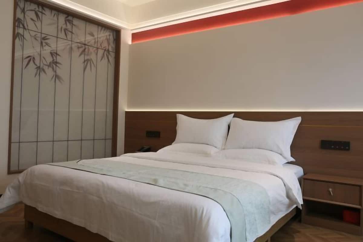 Quarto de hotel com cama grande, mesa de cabeceira e painel de controlo fixado na parede.