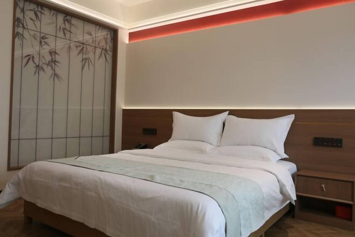 A hotel room with a large bed, a bedside table, a nightstand, and a wall-mounted control panel.