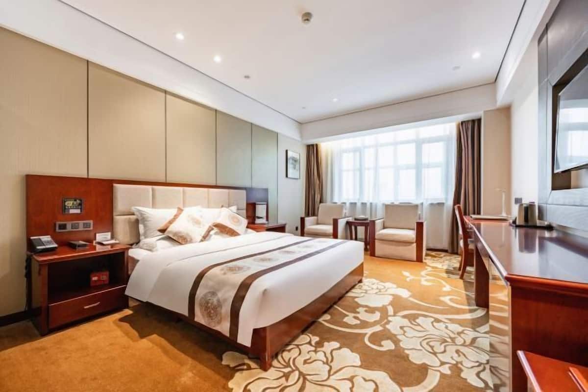 Quarto de hotel com uma cama grande, uma escrivaninha, uma cadeira e uma televisão.