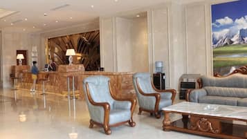 A hotel lobby with a reception desk, two armchairs, a sofa, and a large painting.