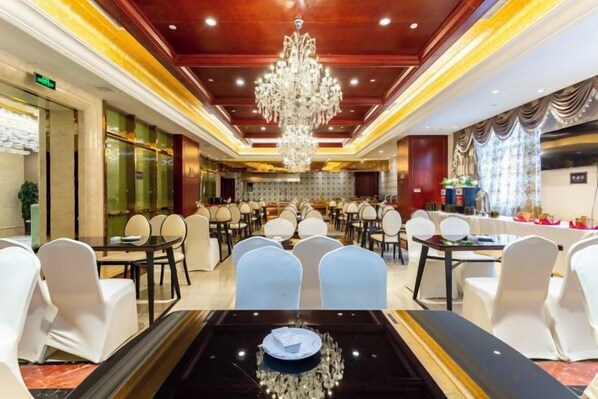 A hotel dining area with round tables, white chairs, and a chandelier.