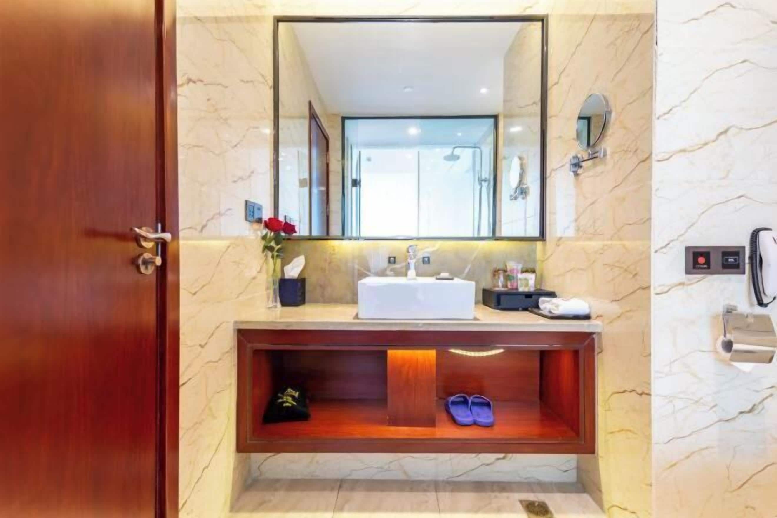 Une salle de bain avec un mur en marbre, un meuble-lavabo en bois, un grand miroir, une douche et un porte-serviettes.