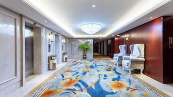 Ein Hotelkorridor mit Teppichmuster, einem Kronleuchter und Sitzbereichen.