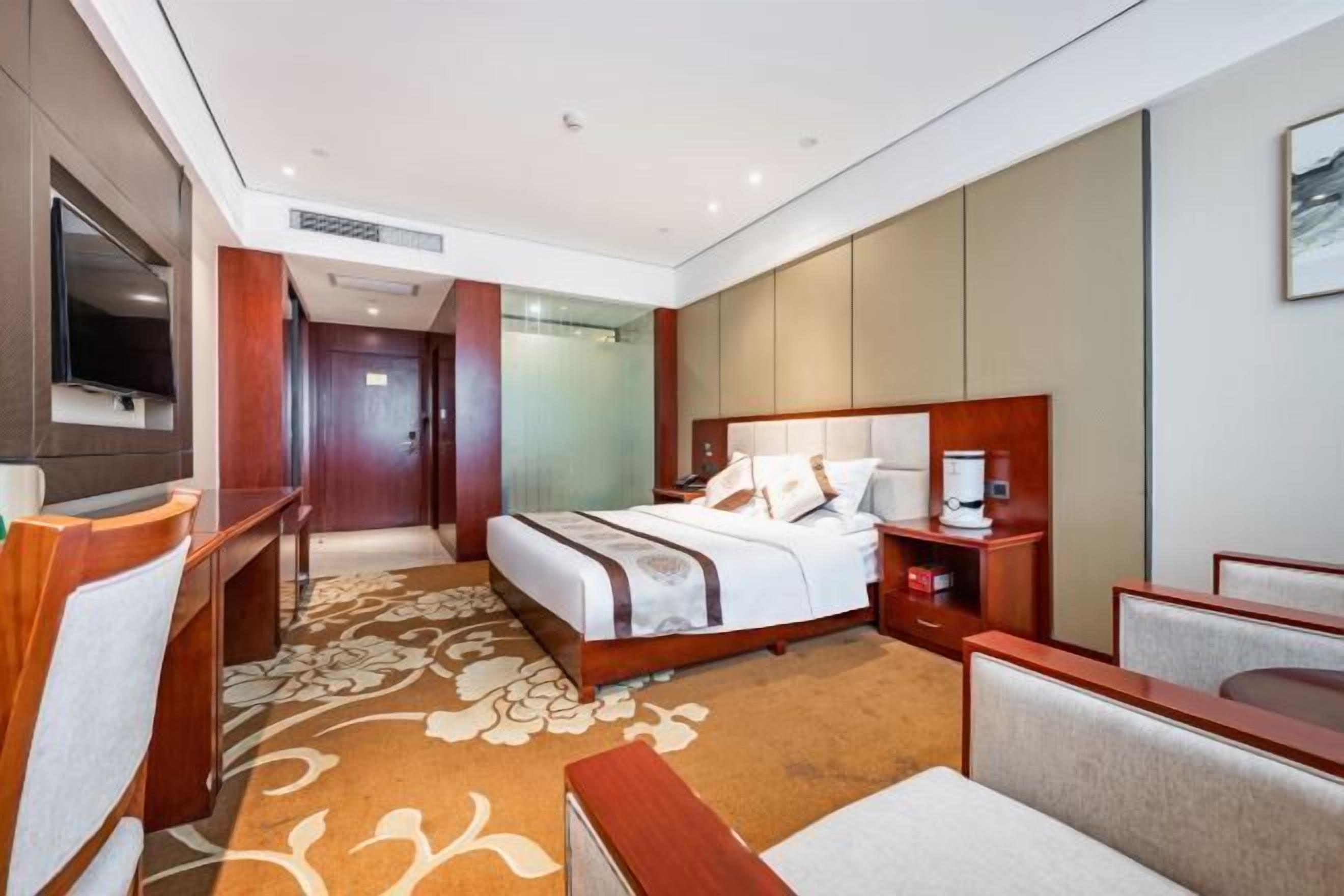 A hotel room with a bed, a desk, a TV, and a shower.