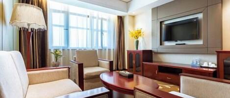 A hotel room with a TV, seating area, and a window with curtains.