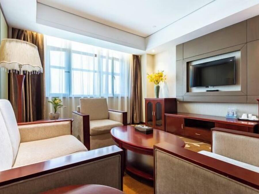 Quarto de hotel com televisão, área de estar e janela com cortinas.