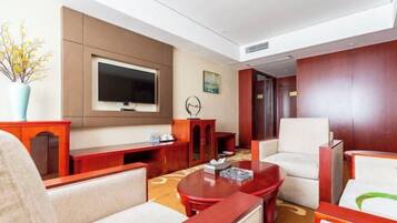 A hotel room with a flat-screen TV, a sofa, a chair, a coffee table, and a decorative vase.