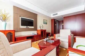 A hotel room with a flat-screen TV, a sofa, a chair, a coffee table, and a decorative vase. - Guoluo Hotel (Xining)