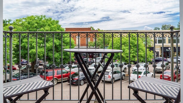 Ein Balkon mit Tisch und Stühlen, der auf einen Parkplatz mit verschiedenen Autos und einem Gebäude im Hintergrund blickt.