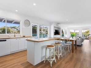 A modern kitchen with white cabinetry, a wooden countertop, and a large island with bar stools. - Rye Baby by Ready Set Stay- Main & Guest House (Rye)