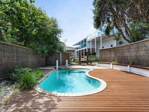 A swimming pool with a wooden deck, surrounded by a high wall and trees. - Rye Baby by Ready Set Stay- Main & Guest House (Rye)
