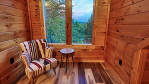A cozy cabin room with a wooden interior, a window with a view of trees, a patterned sofa, and a small round table. - Fire pit, family fun, clean, great location, comfortable cabin on 1.5 acres (Pigeon Forge)