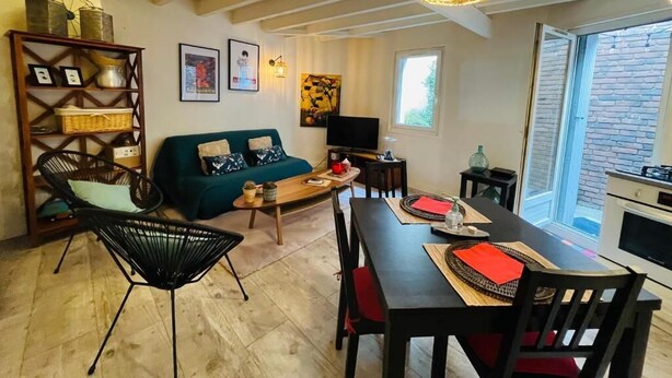 Un salon confortable avec un canapé, une table à manger et des chaises, un téléviseur et une grande fenêtre.
