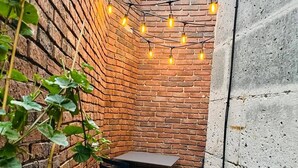 Un mur de briques avec une table et des chaises, des guirlandes lumineuses et des plantes.