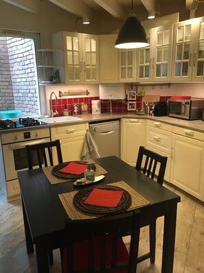 A modern kitchen with white cabinets, a gas stove, a microwave, and a dishwasher. - Charming Town Center House (Angoulême)