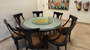A round glass table with a central golden ornament, surrounded by six dark wooden chairs with cushioned seats.