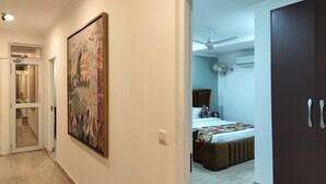 A hallway with a large framed artwork, a door leading to a bedroom with a bed, a ceiling fan, and an air conditioning unit.