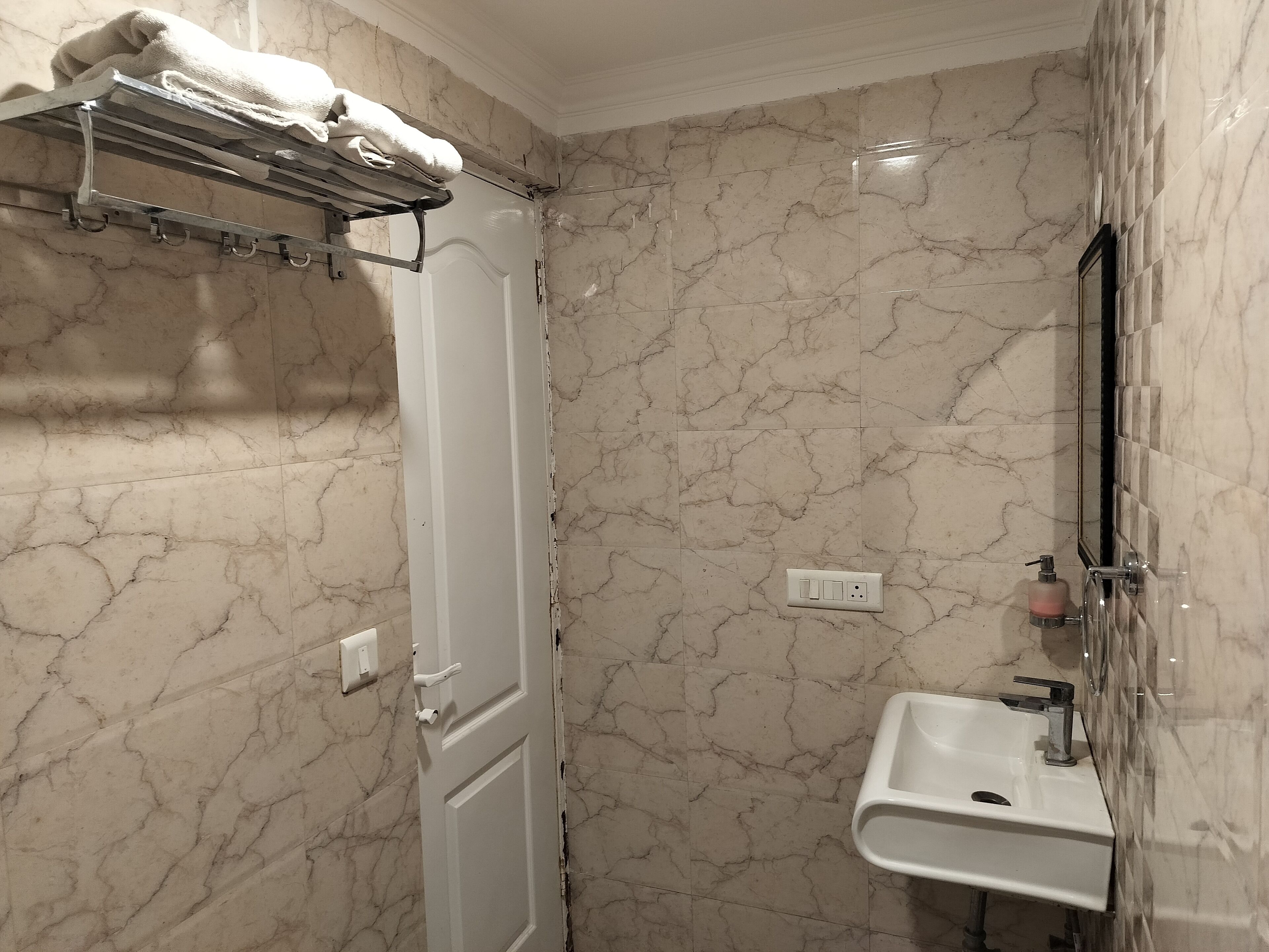 A bathroom with a marble wall, a white door, a towel rack, a sink, and a mirror.
