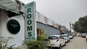 A building with a sign for 'Luxury Rooms' and 'Farmhouse Inn'. There are several parked cars along the street in front of the building.