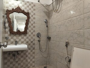 A bathroom with a marble-tiled shower, a sink with a mirror, and a toilet.