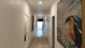 A long, well-lit hallway with a polished floor, framed artwork on the walls, and a large painting of a toucan on the right.
