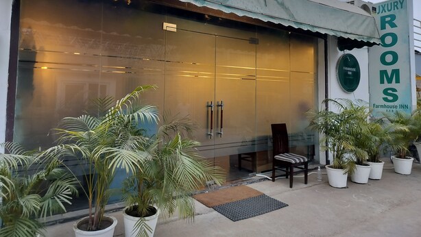 A building with a large glass facade, a sign reading "JXURY ROOMS," and several potted plants in front.