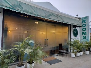 A building with a large glass facade, a sign reading "JXURY ROOMS," and several potted plants in front.