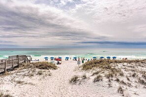 A beach with a wooden walkway leading to the shore, beach umbrellas, and a clear view of the ocean. - Sunny Destin Condo w/ Pool & Beach Access! (Destin)