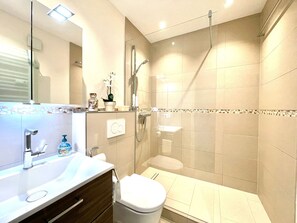 Et badeværelse med bruser, toilet, håndvask og et spejl.