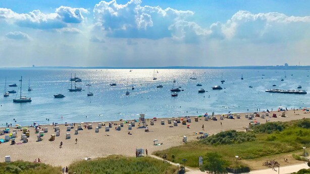 Une plage où l’on peut voir de nombreux bateaux sur l’eau et une zone de plage très fréquentée.
