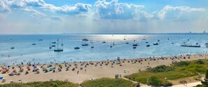 A beach with numerous boats on the water and a crowded beach area.