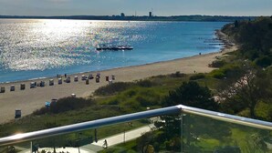 Une vue côtière avec une plage, un bateau et le profil d’une ville lointaine.