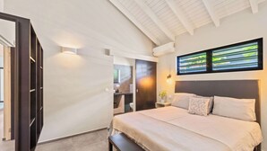 Une chambre à coucher moderne avec un grand lit, un banc, une table de chevet et une lampe fixée au mur.