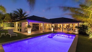 Une maison moderne dotée d’une piscine, d’un espace salon extérieur et d’un patio bien éclairé.