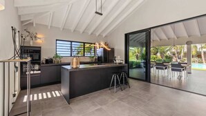 Une cuisine moderne dotée d’un îlot central, de grandes fenêtres et donnant sur une terrasse extérieure.
