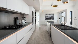 A modern kitchen with white cabinetry, black countertops, and stainless steel appliances. There is a large window providing natural light and a view of the outdoors.