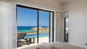A hotel room with a large sliding glass door leading to a balcony with a view of the ocean and a pool.