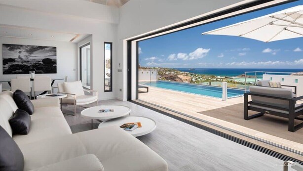 A modern living room with a large window overlooking a pool and ocean view.
