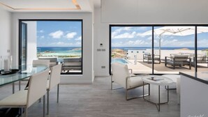 A modern interior with large windows offering ocean views, a glass dining table, and a pool area.