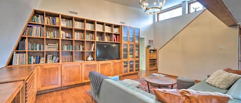 Ein geräumiges Wohnzimmer mit einer großen Bücherwand, einem Fernseher, einem Sofa und einer Holzzieldecke.