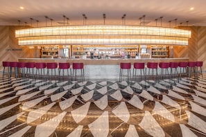 Un espace bar agrémenté d’un lustre moderne, d’un comptoir et de plusieurs tabourets de bar rouges.