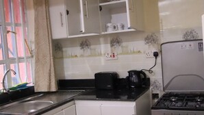 Une cuisine avec des meubles blancs, un plan de travail noir, une cuisinière et une fenêtre avec un rideau.