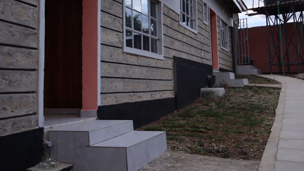 Un bâtiment avec une façade en bois, une porte rouge et un réservoir d’eau en arrière-plan.