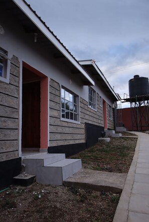 A building with a wooden exterior, a red door, and a water tank in the background. - Stay.Plus Ebony Mara House (Narok)