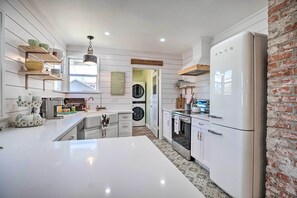 Una cocina moderna con armarios blancos, una isla central, una pared de ladrillo decorativa y una lámpara colgante.