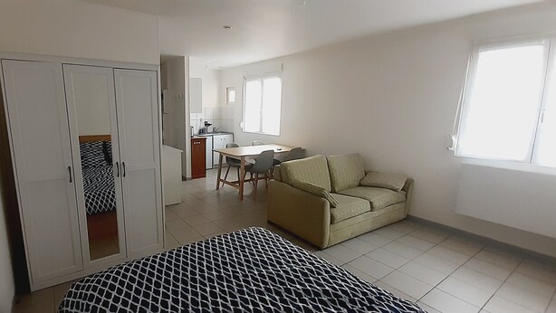 A room with a bed, a sofa, a dining table with chairs, a kitchen area, and a window.
