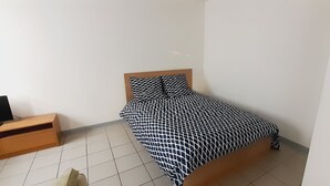 A small, neatly arranged bedroom with a bed, a wooden nightstand, and a television.