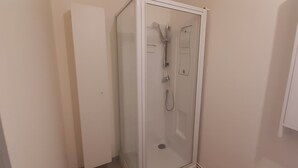 A small, enclosed shower area with a glass door, a showerhead, and a control panel.
