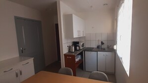 A compact kitchen with white cabinets, a coffee maker, and a sink.